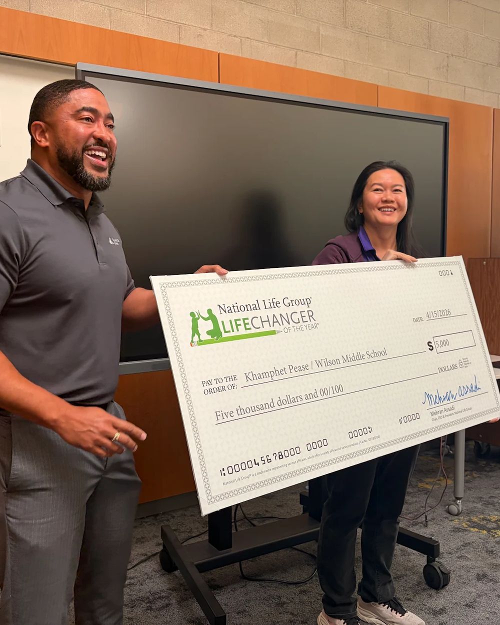 A member of Chris Reid's team presenting an award check to a middle school teacher